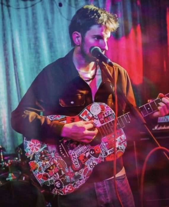 Leland playing guitar with lots of stickers. Colourful light filter is used.