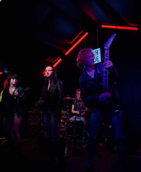 The Obsession Of Scarlet on stage with red neon lights in the background and a lit up "Rough Trade" Sign