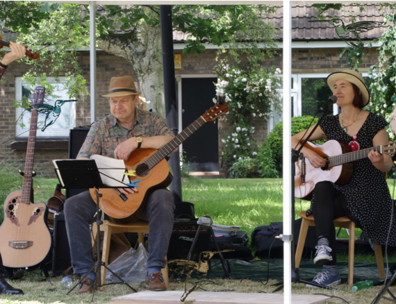 The four members of the Hummingbirds playing outisde on the grass. From left to right, one violinist, one guitarist, one ukele player and another guitarist.