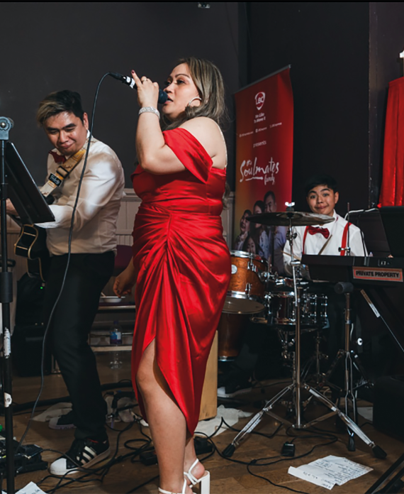 Soulmates family performing on stage. Mum is wearing a red dress and is centre stage with red curtains.